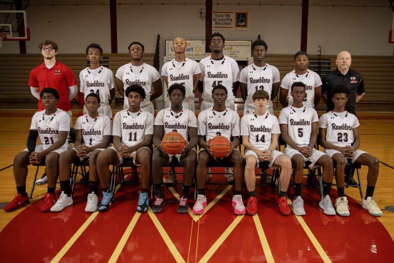 A basketball team stands together in a gym, smiling for a group photo, wearing matching uniforms and basketball shoes.