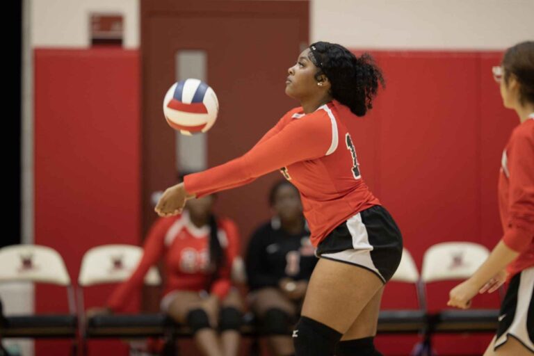 A female volleyball player in a striking red and black uniform, ready to engage in play on the court.