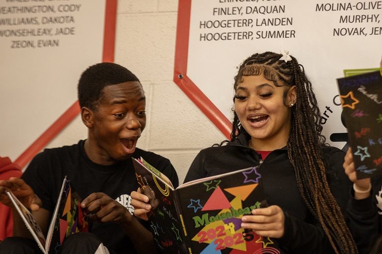 Two students smiling while looking at a yearbook