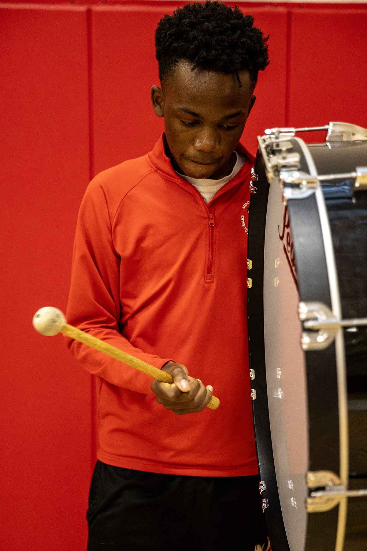 A young man energetically plays a drum in a vibrant red gym, showcasing his musical talent and enthusiasm.